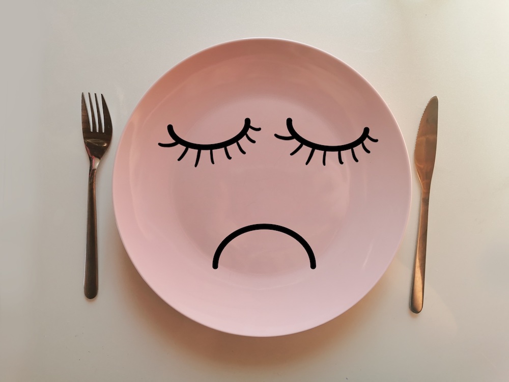 Pink plate and cutlery with sad face on the plate to indicate hunger.