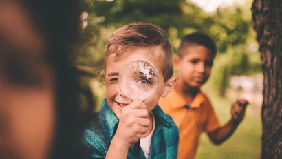 Little boy outside looking through magnifying glass