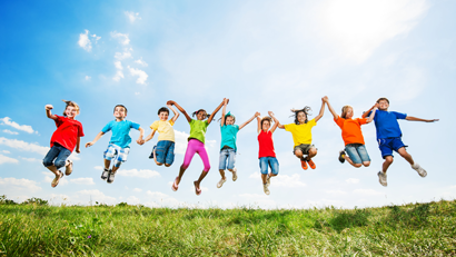 Mixed group of children in colourful clothing jumping on grass