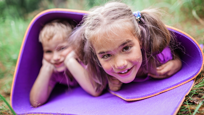 Happy boy and girl playing in a rolled up purple yoga mat outside