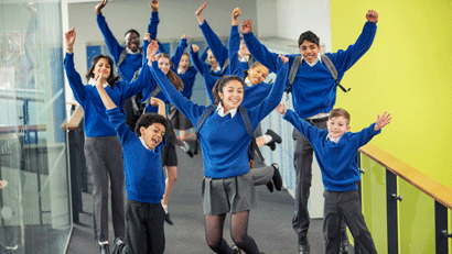 Mixed group of enthusiastic students in uniform jumping in school corridor