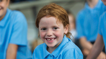 Happy-looking redhaired schoolgirl with missing tooth smiling amid peer group