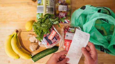 Photo of small pile of groceries with person's hand suggesting they are scrutinising the shopping receipt.