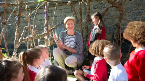 Female teacher and primary school pupils in an outdoor learning space in the school playground.