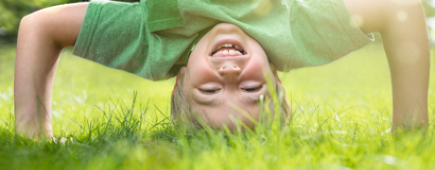 Happy boy doing a headstand on the grass in the summer