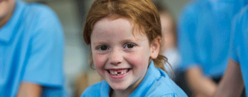 Happy-looking redhaired schoolgirl with missing tooth smiling amid peer group