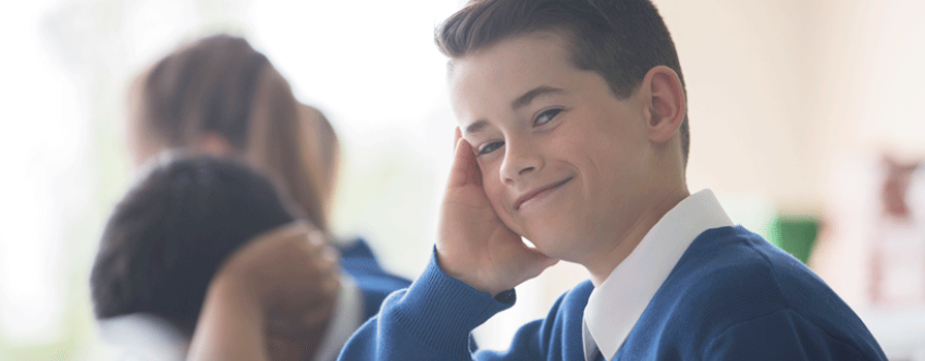 Close-up of primary school boy wearing a blue and white uniform in a classroom, looking assured.