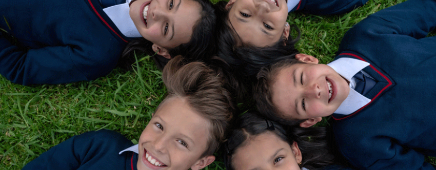 Five school pupils lying on the grass looking happy and relaxed